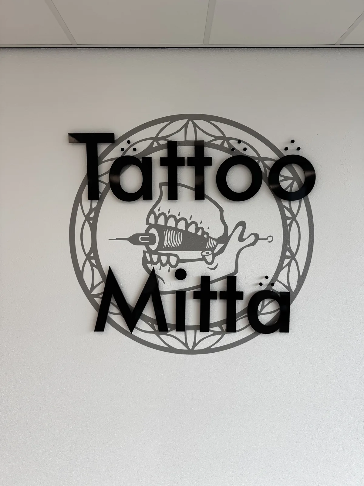 Gemonteerd zwart Tattoo Mitta-logo met afstand tot de witte wand